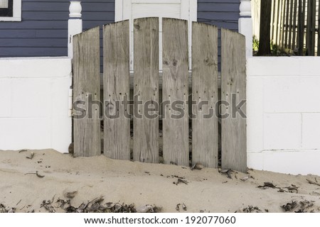 Simplicity of early spring in a beach town: Hinged wooden gate, partially buried in sand, to modest beach house in May, before the arrival of vacationers in southwestern Michigan