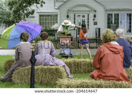 WAUCONDA, ILLINOIS/USA - JULY 12, 2014: Two girls in period dress watch a girl in contemporary summer attire help a magician perform a trick during a reenactment of the American Civil War (1861-1865).