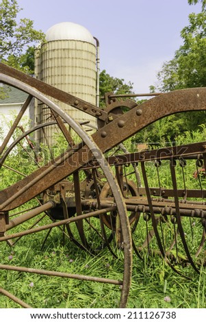 Rural bygones at a glance: Vintage farm machinery stands rusting in grass near silo on public educational farm, summer in northern Illinois