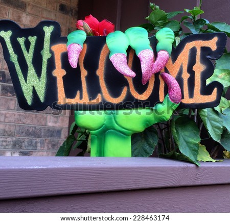 Halloween greeting: Green hand with purple talons gripping a welcome sign on balcony
