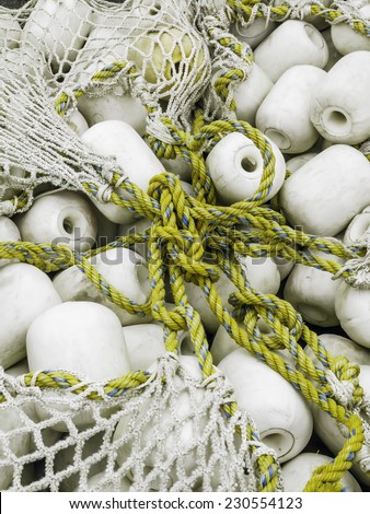 Togetherness at a glance: Knotted yellow lines and white fishing net holding white floats together in temporary storage in marina