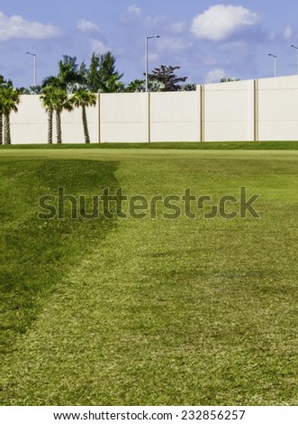 High concrete wall built to stop errant golf balls before they can hit people or vehicles passing by dogleg of golf course in Florida