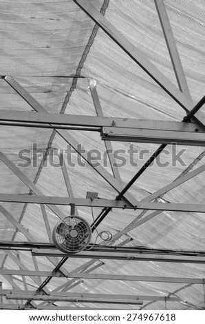 Electric fan on rafter by roof of greenhouse, in black and white