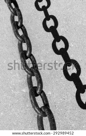 Synergistic strength in black and white: Part of crowd control barrier chain above its dark shadow on concrete