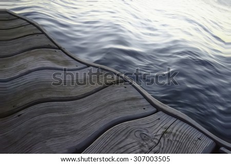 Under the influence: Wavy wooden dock by water reflecting light from the rising sun, for themes of fluidity or altered states of mind
