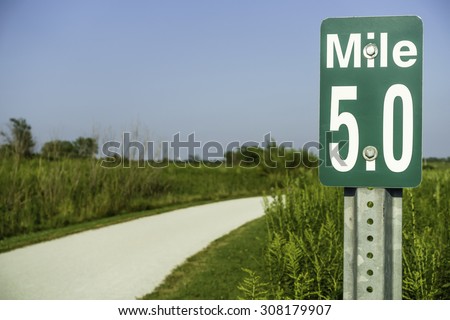 Marker at mile 5 by gravel path across prairie preserve for joggers, bicyclists, and hikers in west suburban Chicago, USA, in summer