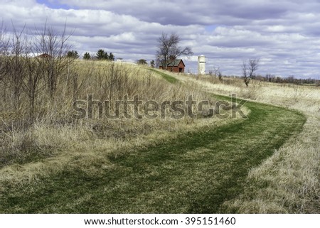 GENEVA, ILLINOIS/USA - MARCH 20, 2016: Part of an historic farmstead is seen beyond a grassy bend in Lake View Trail at Peck Farm Park, a 385-acre nature retreat in this far western suburb of Chicago.