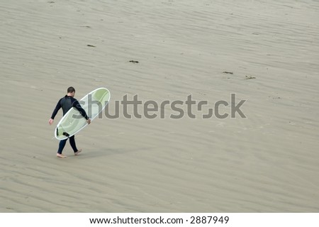 Adult male surfer carries stylish surfboard across sandy beach toward shallow waves