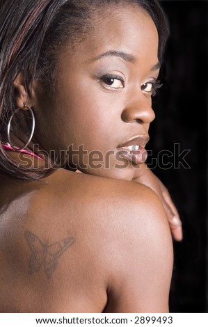 Young black woman looking over her bare shoulder (butterfly tattoo) at you