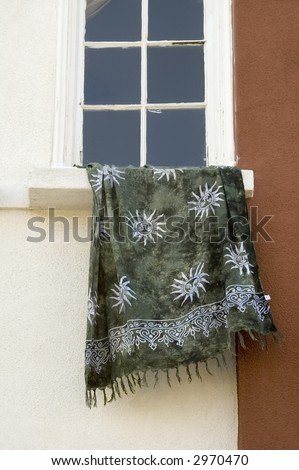 Fringed towel with sun pattern hanging off ledge of plain window