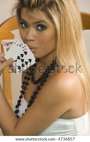 Pretty young Asian-American woman with blonde hair and black bead necklace shows a hand of playing cards