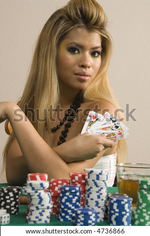Pretty young Asian-American woman with blonde hair shows hand of cards by stacks of poker chips and drink