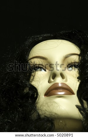 Face of female Caucasian mannequin wearing black wig in store window, sunset, close-up from below