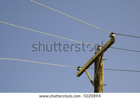 Top of utility pole with three power lines against blue sky at sunset