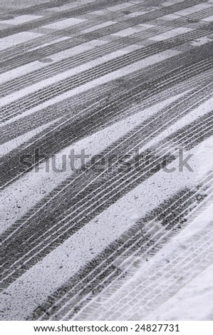 Multiple tracks of car tires, with a few footprints, in snow on pavement