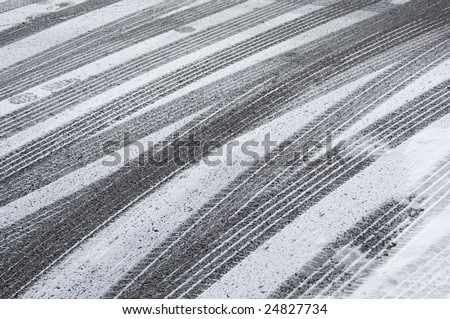 Multiple tracks of car tires, with a few footprints, in snow on pavement