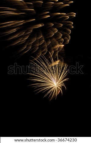 Spidery yellowish-white burst of fireworks underneath glowing embers from previous explosion