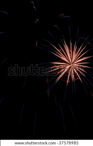 Pinkish-white burst of fireworks amid short blue streaks from previous burst