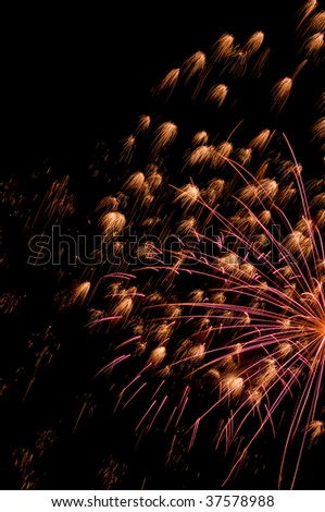 Reddish streaks from off-camera burst of fireworks amid many small bursts like prairie flowers