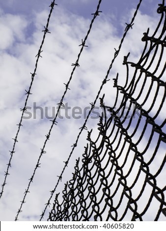 Keep out -- chain link fence with barbed wire against partly cloudy sky