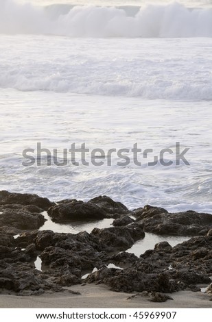 Waves approach tide pools on volcanic rock -- focus on tide pools