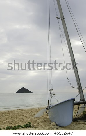 Partial view of small sailboat on beach, with offshore island and sunbeams through overcast sky