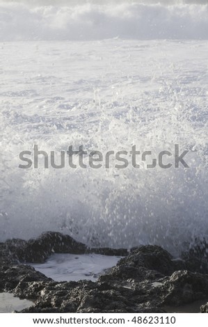 Wave crashes against volcanic rock with tidal pool, with another wave on the way