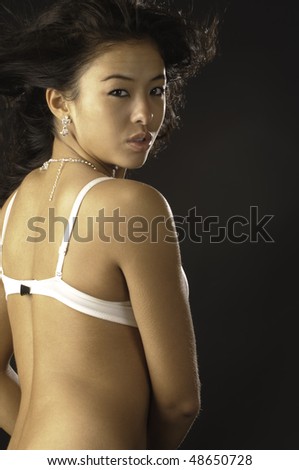 Over-the-shoulder shot of young Asian-American brunette in white brassiere and jewelry, with goosebumps