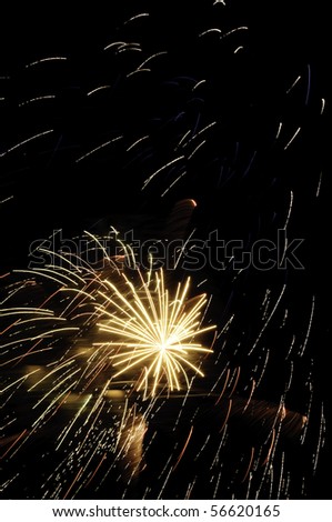 Yellow-white embers falling all around small white-hot burst of fireworks with puffs of smoke