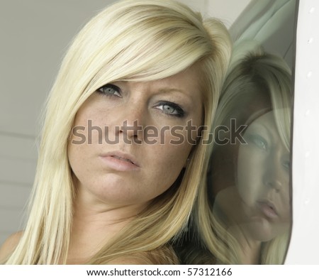Head shot of young blonde Caucasian woman with freckles and her reflection in window of airplane in hangar