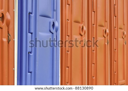 Row of plastic doors to portable toilets, one blue and the others red