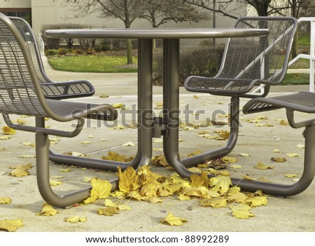 Autumn at a glance on college campus: Leaves blown against round table with four identical seats on plaza of community college in northern Illinois, mid November