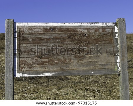 Your message here: Weathered wooden sign, blank, with little paint left, on hillside under  clear blue sky