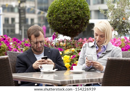 Young Couple Having Coffee In Street Cafe Busy With Their Mobiles