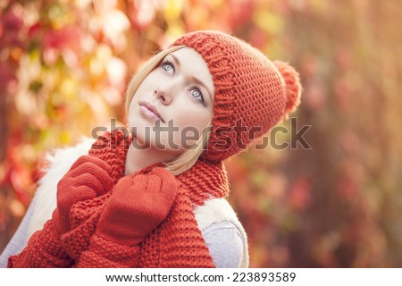 portrait of beautiful woman dressed in red knitted hat scarf and gloves against colorful leafy background