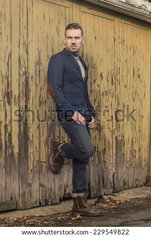 portrait of handsome young man dressed in jeans blazer and military boots posing against old garage doors