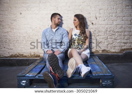 young couple sitting on a pallet against brick wall