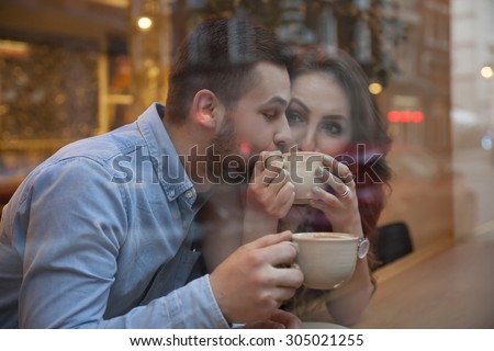 shot through the shopwindow young couple drinking coffee in cafe