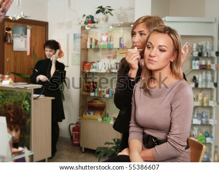 beautician making up young woman\'s face in salon