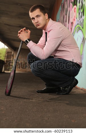 young guy with baseball bat sitting under bridge