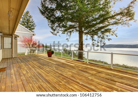 Large wood porch with glass railings and water view.