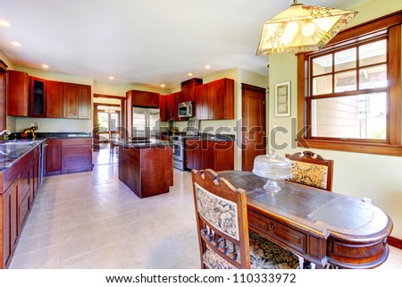 Large chery wood kitchen with dining room table and tile floor.
