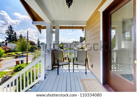 Front door entrance with steps and two chairs under covered porch.