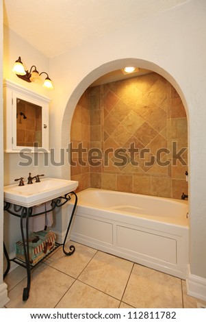 Tub with arch and stone tiles and sink natural bathroom design.