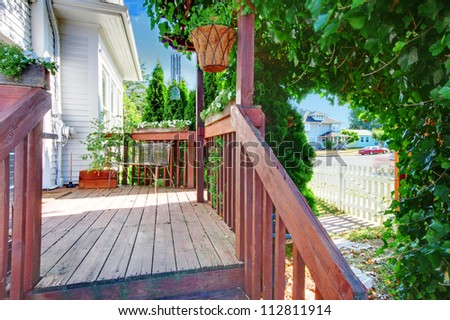 Small old deck with fence and white house and green bush.