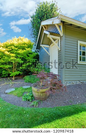Grey small outdoor shed with backyard landscape with green summer grass.