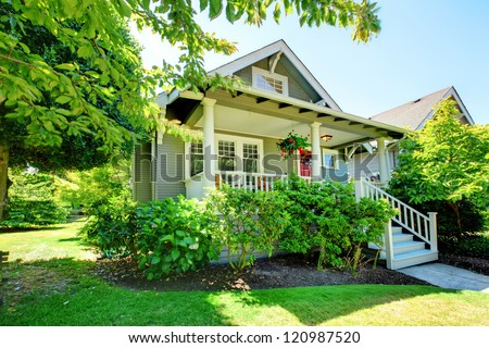 Grey Small House With Porch And White Railings With Summer Landscape.