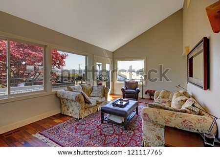 Large living room with two sofas and red rug with many windows.