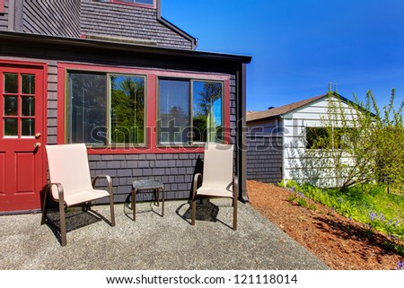 Two chairs next to red door and small black house with shed on the side.