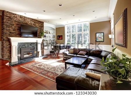 Luxury living room with stone fireplace and leather sofas, cherry hardwood and nice rug.